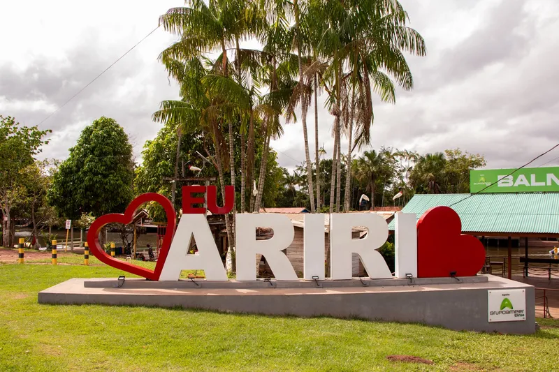 "Eu Ariri" letter sign with red hearts on a lawn, surrounded by palm trees, next to the green roof of the bathing area.