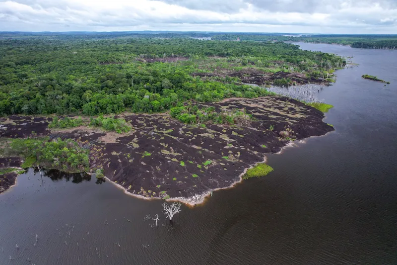 Vista aérea de la Cidade das Pedras: gran laja oscura que avanza en el río Araguari, rodeada de selva y árboles secos en el agua