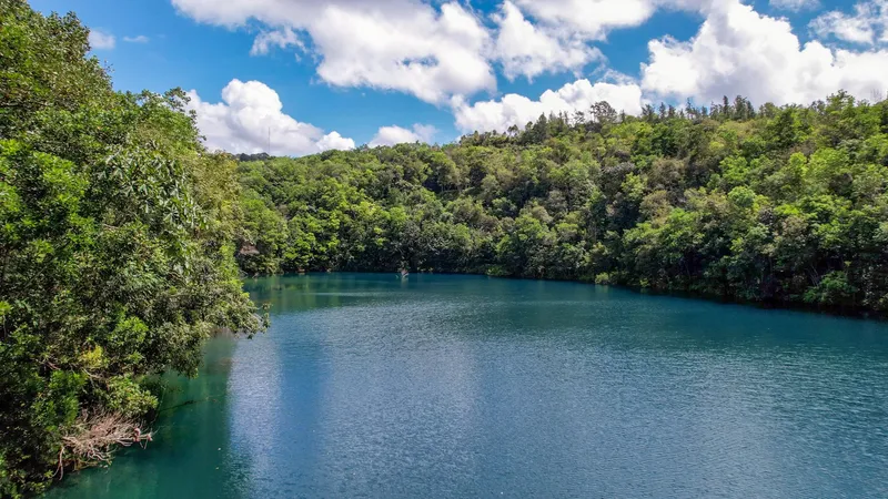 Lagoa Azul in Serra do Navio with blue-green water surrounded by densely forested hills under a blue sky with clouds.