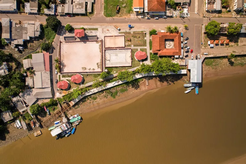 Vista aérea cenital del paseo de Mazagão Novo, con canchas, quioscos de techo rojo, pasarela y barcos en el río turbio.