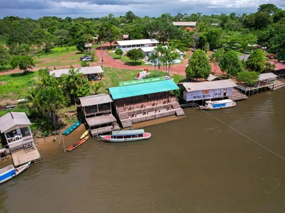 Aerial view of Balneário do Ariri, with a green roof, wooden structures and boats along the bank.