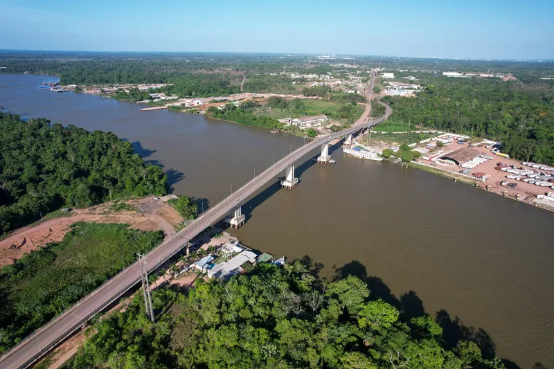 The Ponte da Integração over the Matapi River from above, with the highway running through forest and a truck yard on the bank.