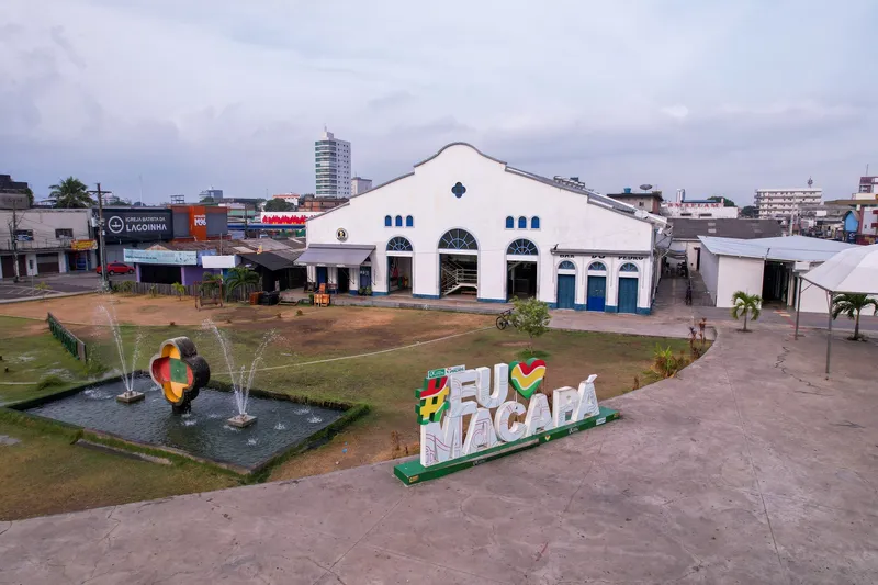 Aerial view of the Mercado Central de Macapá with a fountain in front and an "Eu amo Macapá" sign in the square, cloudy sky.
