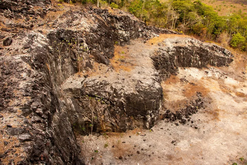 Paredes de roca oscura y grava clara en la Montanha da Pluma vistas desde arriba, con vegetación seca y bosque al fondo