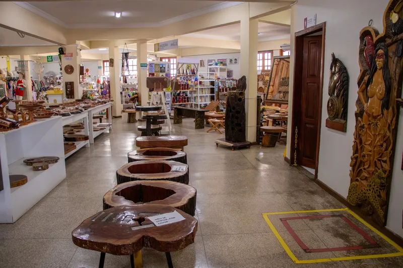 Aisle in Casa do Artesão with a row of wooden trunk tables and large carved sculptures on the wall.