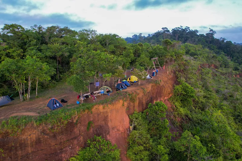 Aerial view of the camp at the Mina F12 lookout: colorful tents atop a red earth cliff surrounded by forest.