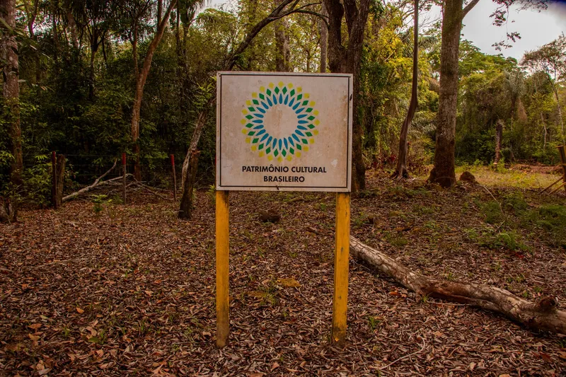 Placa de Patrimônio Cultural Brasileiro na entrada do sítio das ruínas da primeira igreja de Mazagão Velho, em meio à mata.