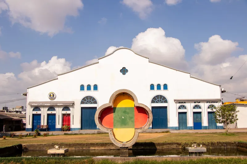 White facade of the Mercado Central de Macapá with blue doors and a colorful flower-shaped sculpture over a reflecting pool.