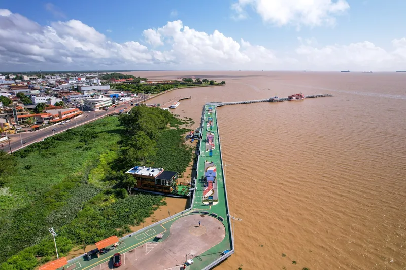 Vista aérea del Píer do Santa Inês sobre el río Amazonas de aguas turbias, con paseo verde, zona de vegetación y la ciudad a la izquierda.