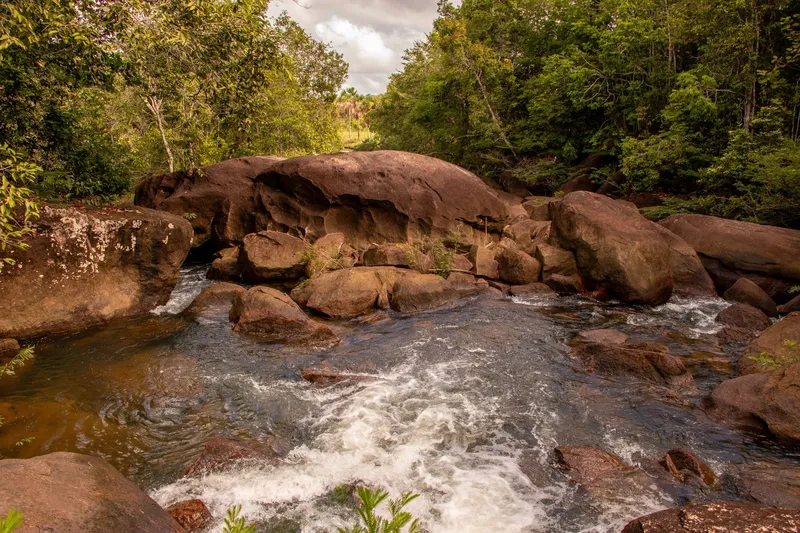 Agua corriente y espumosa entre grandes rocas redondeadas en la Cachoeira do Pium, con bosque denso en las orillas