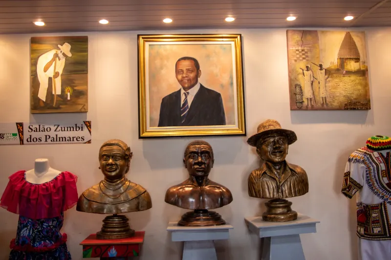Salão Zumbi dos Palmares no Museu Afro-Amazônico: três bustos de bronze em pedestais diante de quadros, com um retrato emoldurado ao centro.