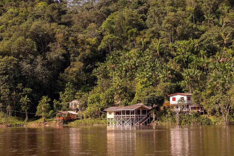 Colorful stilt houses on the bank of the Amapari River, in the Pedra Preta community, at the foot of a forested hill.