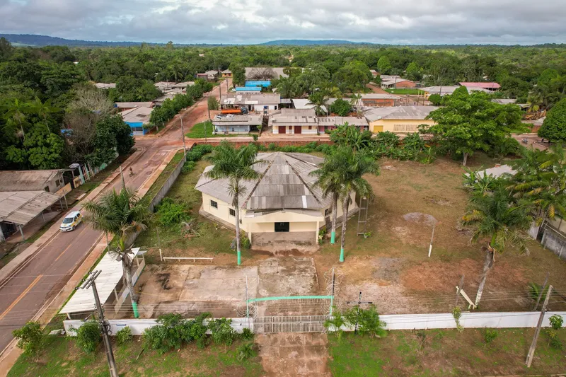 Vista aérea da Igreja Nossa Senhora do Perpétuo Socorro em terreno murado com palmeiras, ao lado de uma avenida, com casas e mata ao fundo.