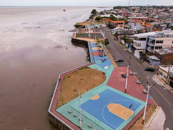 Vista aérea da orla de Cidade Nova, com quadra azul, passeio junto ao rio e casas.