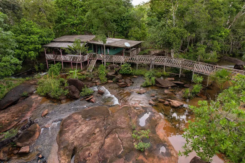 Aerial view of Cachoeira do Traíra: wooden house and walkway over the river among rocks and forest