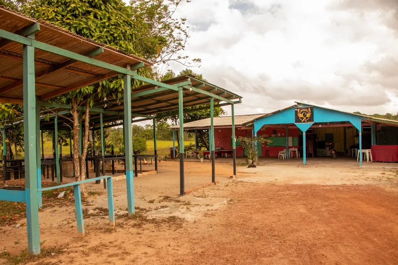 Covered kiosks with a blue frame and the main hall of Balneário Asa Aberta, on red dirt ground