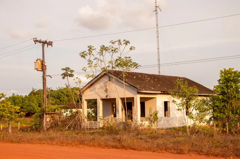 Ancien bâtiment de plain-pied abandonné de la base aéronavale d'Amapá, avec véranda à piliers, végétation envahissante et pylône métallique, sous la lumière dorée du soir
