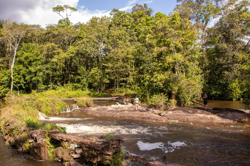 Rápidos del Balneário Ilha do Amor con laja de piedra, pequeñas caídas y dos personas sobre las rocas, selva densa al fondo