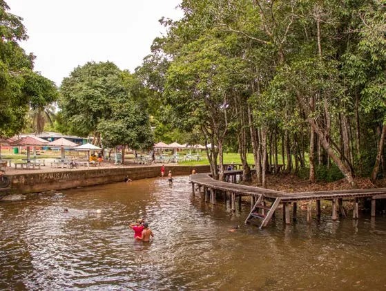 Bathers in the water at Balneário São Joaquim do Pacuí, beside wooden platforms and trees.