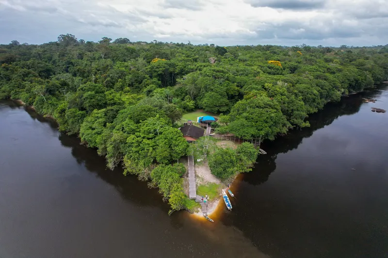 Vista aérea de una base en la punta de tierra entre dos brazos del río Araguari, con casa, muelle y barcos, rodeada de selva