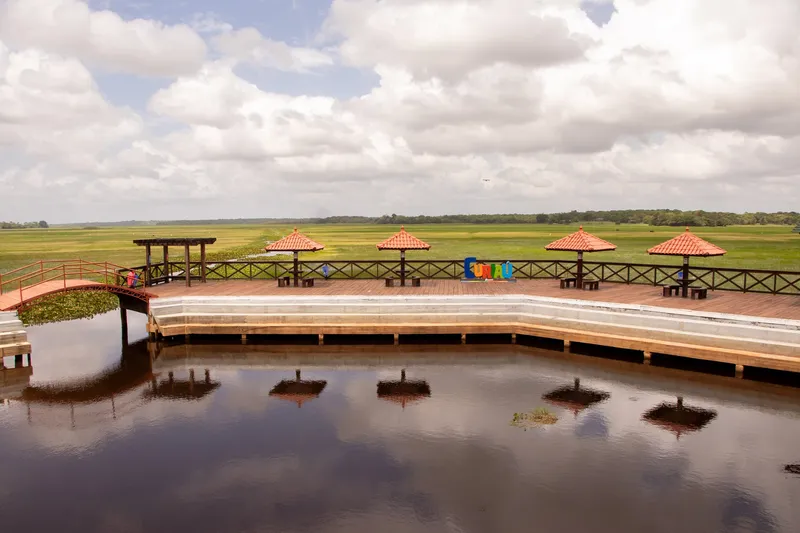 Muelle con sombrillas de tejas y letrero "Curiaú" frente al campo inundado, reflejados en el agua