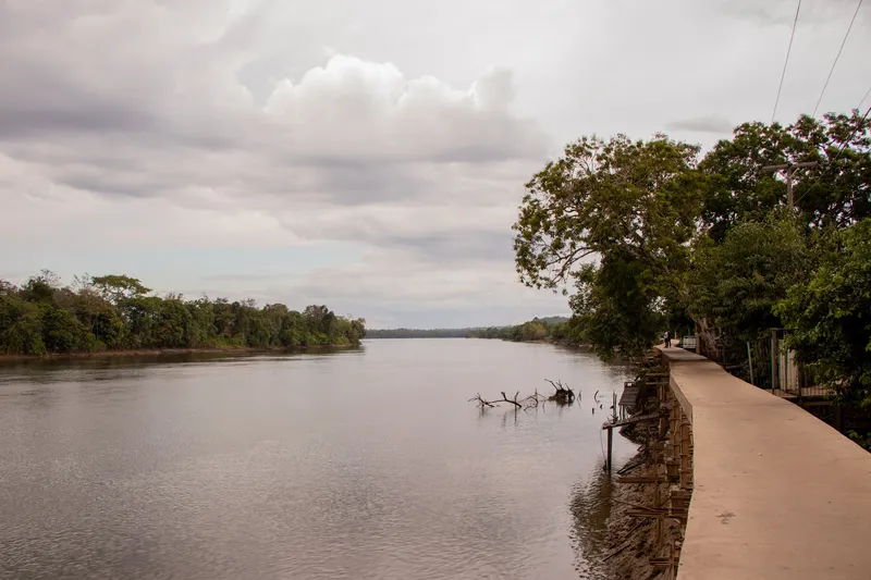 Riverside walkway near Praia da Samaúma, with trees on the bank and cloudy sky