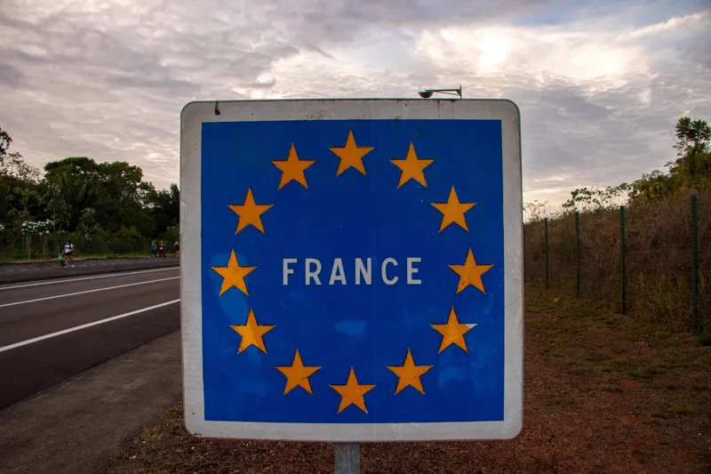 Blue sign with yellow stars and the word France beside the road, marking the arrival on the French side of the border
