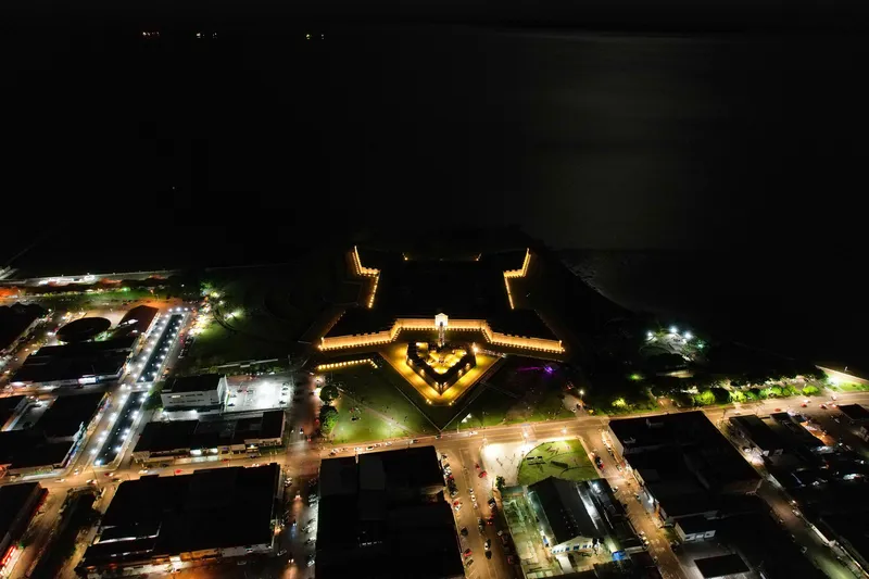 Vista aérea noturna da Fortaleza de São José de Macapá com o contorno em estrela iluminado e as ruas da cidade ao redor.
