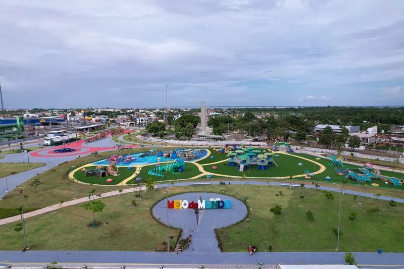 Vista aérea del Parque Meio do Mundo con su letrero, céspedes, zona de juegos temáticos y espejo de agua, y un obelisco al fondo.