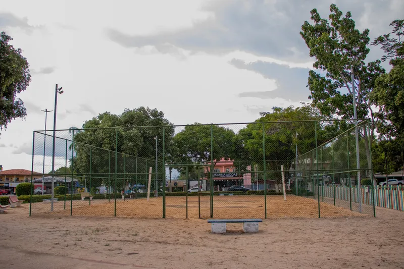 Sand court enclosed by wire fencing in Praça João da Silva Nery, with trees around