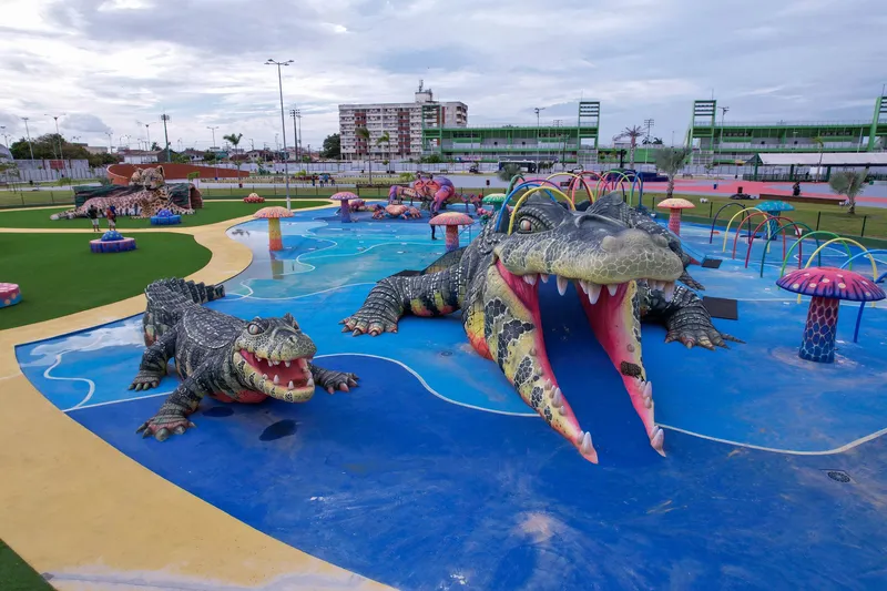 Zona acuática del Parque Meio do Mundo con caimanes gigantes de boca abierta, hongos coloridos y arcos de agua sobre piso azul.