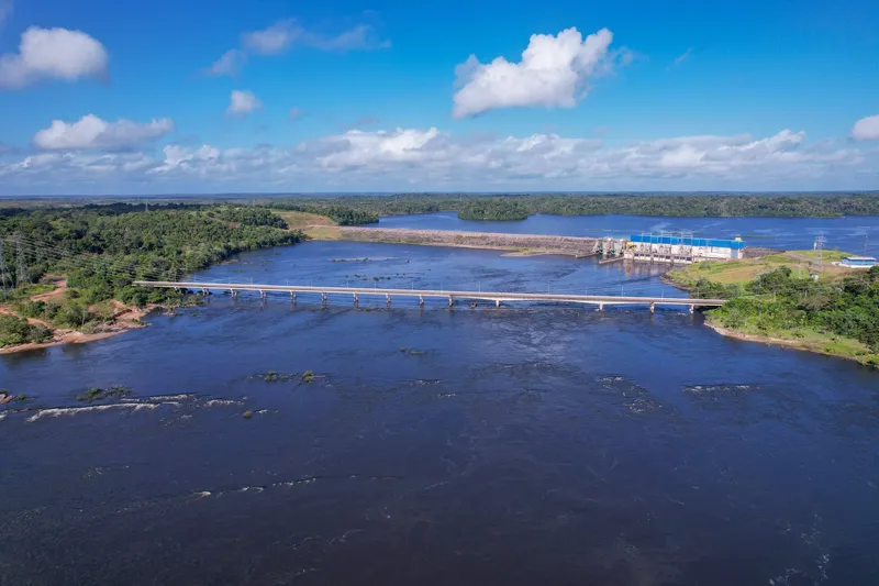 Aerial view of Ponte Tancredo Neves over the wide river, with the hydroelectric plant and dam behind, blue sky