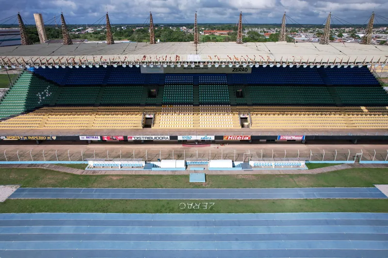 Tribuna cubierta del Estádio Zerão con asientos azules, verdes y amarillos, vista de frente sobre la pista azul.