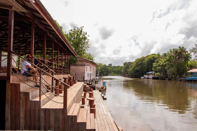 Stepped wooden deck of Balneário do Ariri along the dark river, with forest and floating houses in the background.