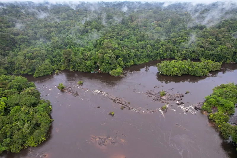 Vista aérea de un río con franja de piedras y pequeños rápidos entre islas de selva, con neblina sobre el bosque en Tumucumaque.
