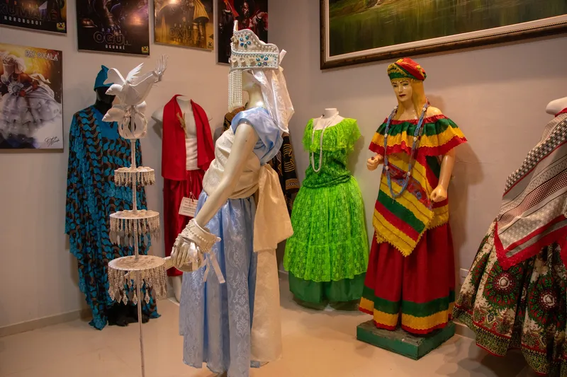 Manequins com trajes afro-brasileiros coloridos no Museu Afro-Amazônico Josefa Pereira Laú, com quadros de orixás na parede ao fundo.