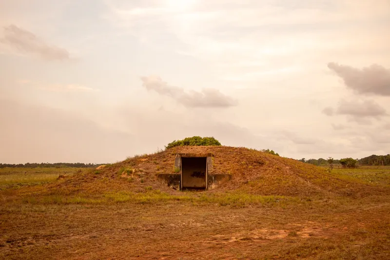Abri en béton à demi enterré sous un monticule herbeux de la base aéronavale d'Amapá, avec entrée rectangulaire et ciel rosé de fin d'après-midi
