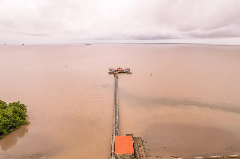 Vista aérea del muelle Eliezer Levy en línea recta hacia el río Amazonas, con barcos en el horizonte y vegetación a la izquierda.