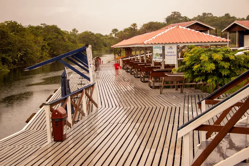 Wet wooden deck by the river at Paraíso da Sereia, with tables under a roof and forest behind