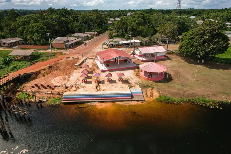 Vista aérea do Balneário Gurupora: salões e quiosques cor-de-rosa, arquibancada colorida à beira do rio escuro e mata ao redor