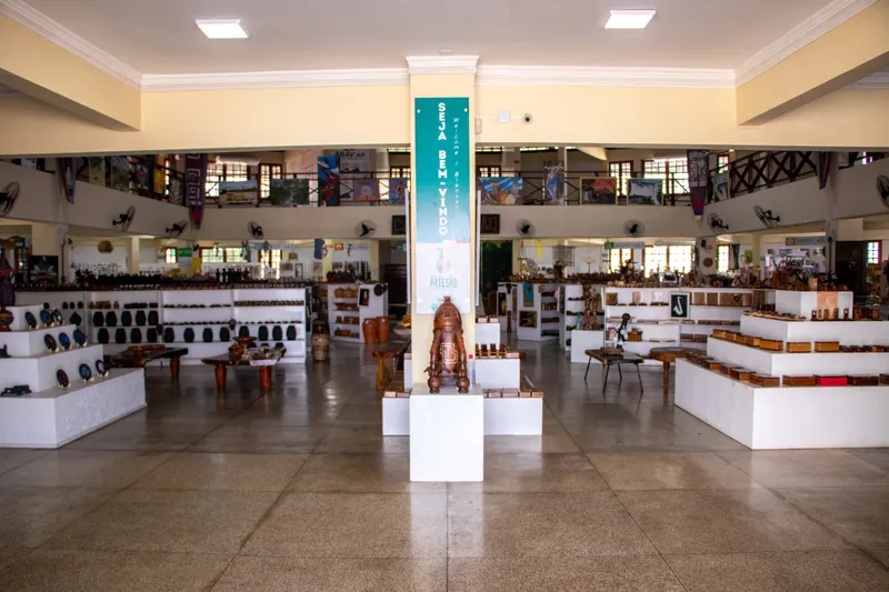 Main hall of Casa do Artesão Amapaense with white displays of wood and ceramic pieces and a mezzanine behind.