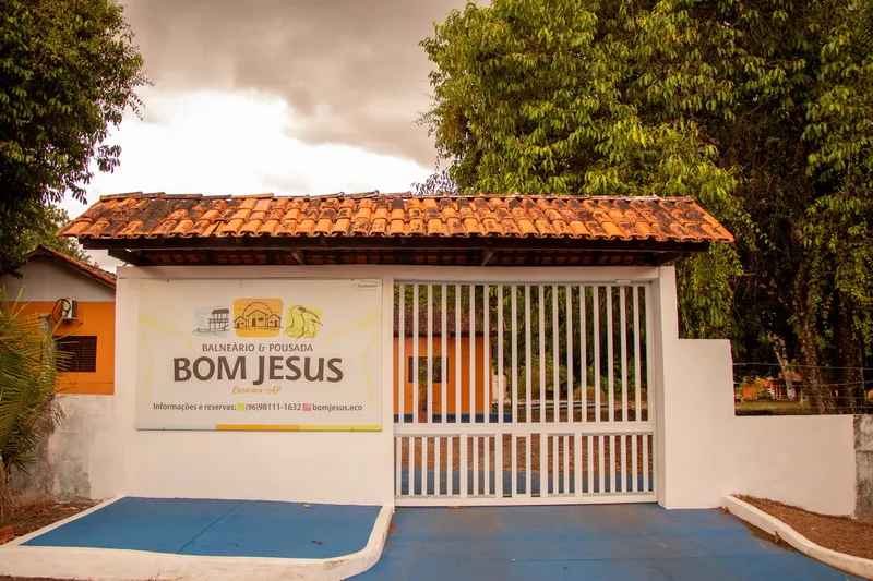 Portão de entrada do Balneário e Pousada Bom Jesus, com placa, muro branco e telhado de telhas