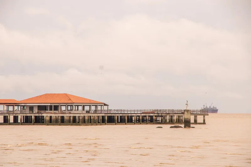 Extremo del muelle Eliezer Levy con techo de tejas sobre el río Amazonas, con un barco al fondo y cielo nublado.