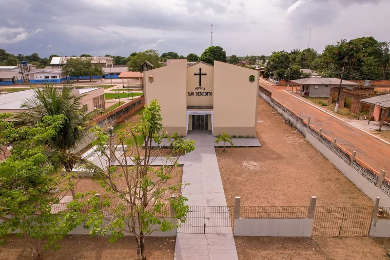 Fachada da Igreja São Benedito de Itaubal vista do alto: paredes bege, cruz, caminho até o portão e rua de terra