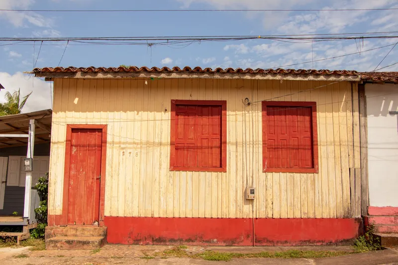 Casa antiga de madeira em Mazagão Velho, pintada de amarelo com porta e janelas vermelhas e telhado de cerâmica.