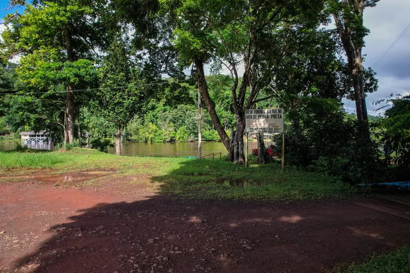 Welcome sign for Balneário Pedra Preta among trees, with the Amapari River behind and red dirt ground.