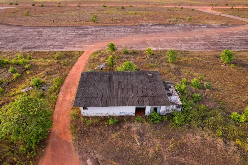 Vue aérienne de la base aéronavale d'Amapá : ancien hangar au toit sombre dans la végétation, chemin de terre rouge et piste en béton fissurée au fond