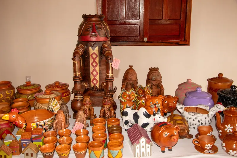 Ceramic pieces on display at Casa do Artesão de Mazagão: a large figure with graphic patterns, pots, cups, piggy banks and clay animals.